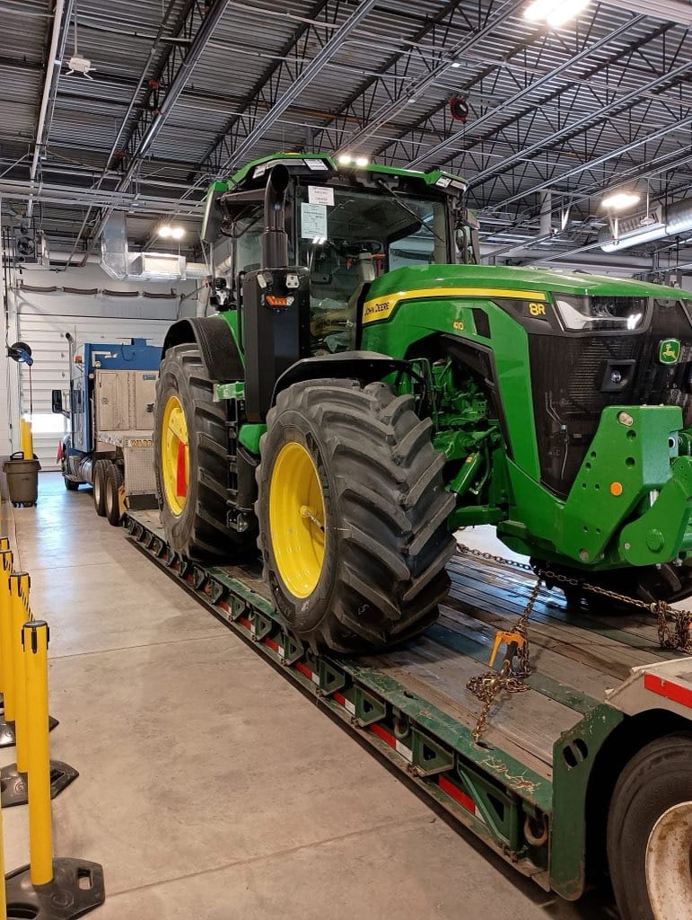 John Deere 8R tractor loaded on a lowboy trailer inside warehouse